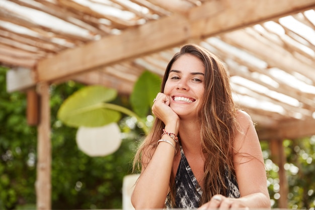Heureux beau femme brune avec un sourire joyeux dans un restaurant confortable, bénéficie d'un temps chaud d'été, d'être en pleine forme après la procédure de spa