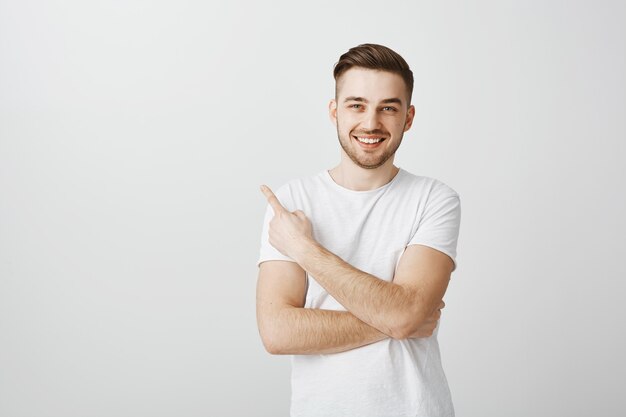 Heureux beau jeune homme en t-shirt blanc pointant le doigt dans le coin supérieur gauche