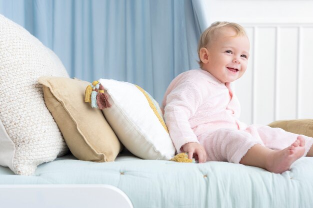 Heureux bébé assis sur un lit et souriant