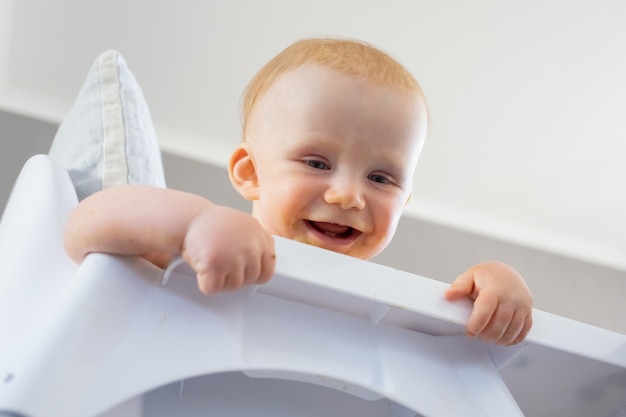 Heureux bébé aux cheveux rouges regardant le sol de la chaise haute, souriant et riant. Faible angle. Processus d'alimentation ou concept de garde d'enfants