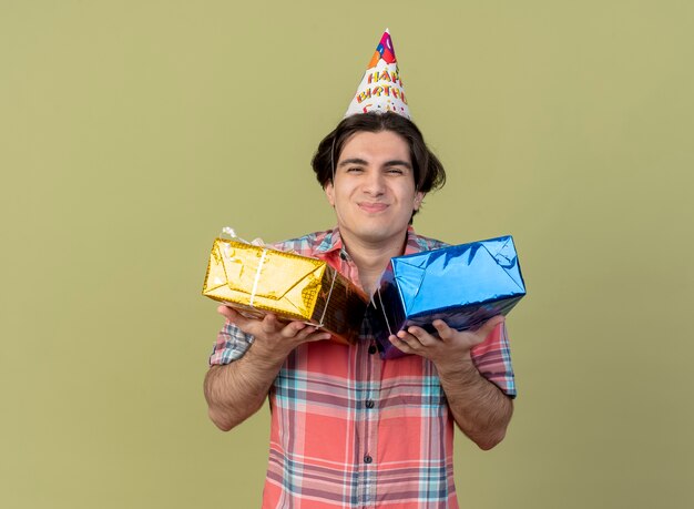 Heureux bel homme caucasien portant une casquette d'anniversaire détient des coffrets cadeaux