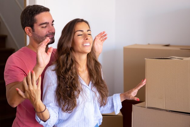 Heureux bel homme menant sa petite amie avec les yeux fermés dans leur nouvel appartement avec des boîtes en carton