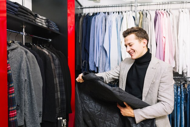 Heureux bel homme regardant veste dans le magasin de vêtements