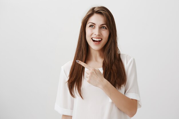 Heureux belle femme pointant et regardant le coin supérieur gauche avec un sourire heureux