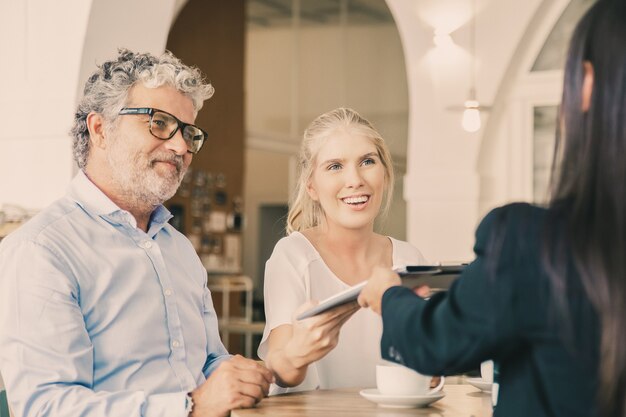 Heureux clients jeunes et matures rencontrant l'agent et lui donnant un contrat d'assurance signé