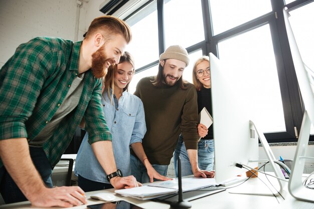 Heureux collègues debout au bureau à l'aide d'ordinateur