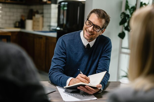 Heureux conseiller financier communiquant avec un couple et prenant des notes dans son carnet