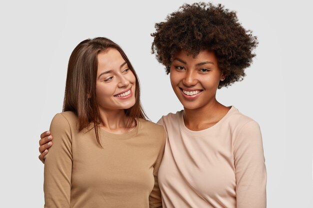 Heureux copines heureux posant contre le mur blanc