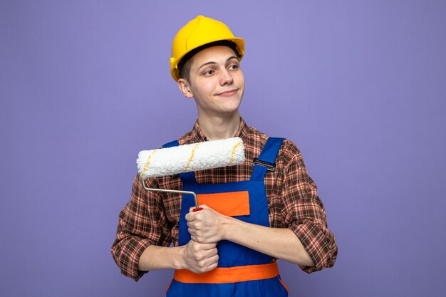 Heureux côté jeune constructeur masculin portant l'uniforme tenant une brosse à rouleau
