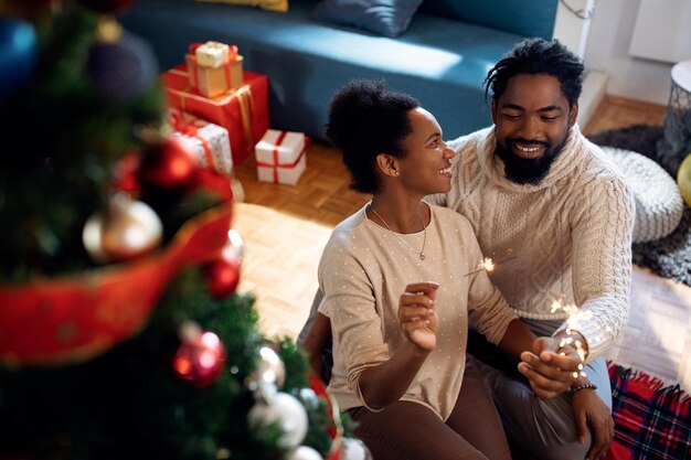 Heureux couple afro-américain s'amusant avec des cierges magiques le jour de Noël à la maison