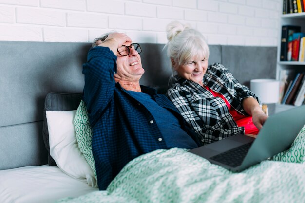 Heureux couple âgé au lit avec un ordinateur portable