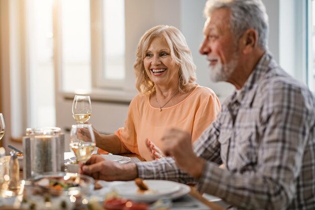 Heureux couple d'âge mûr buvant du vin pendant le déjeuner à la table à manger L'accent est mis sur la femme