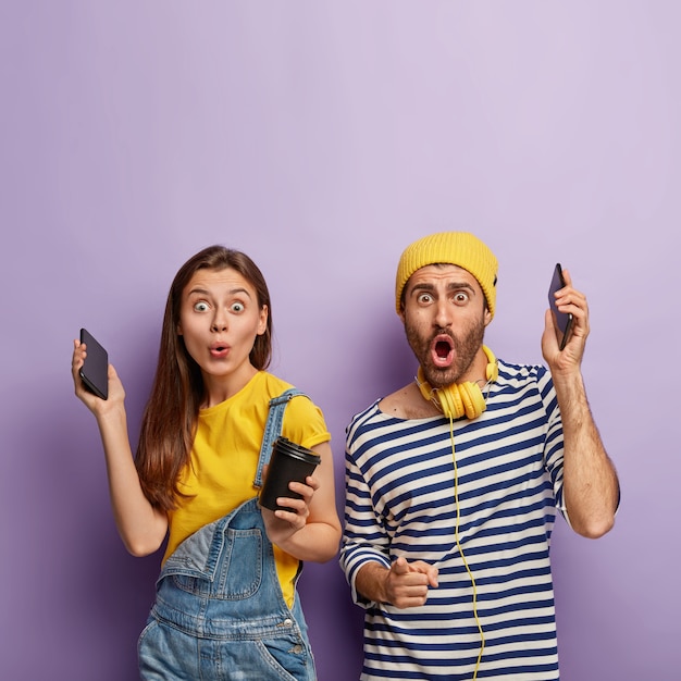 Heureux couple agréable surpris s'amuser ensemble, lever la main avec les smartphones, écouter de la musique agréable, boire du café, profiter du temps libre,