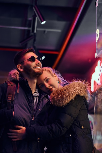 Heureux couple amoureux. Une belle fille étreignant son petit ami debout dans la nuit dans la rue. Enseignes lumineuses, néons, luminaires.