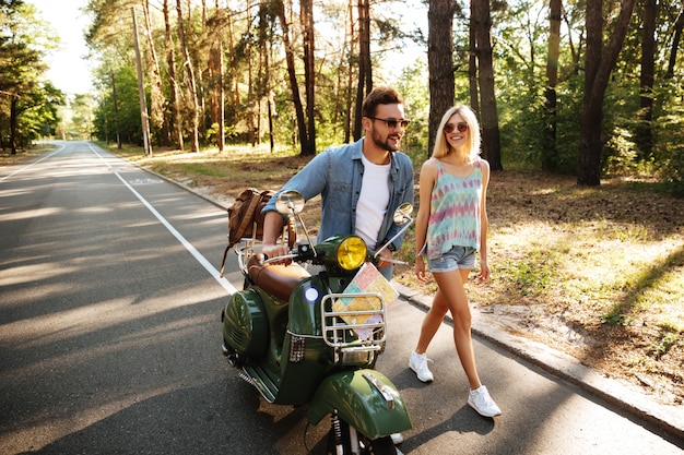 Heureux couple d'amoureux marchant avec scooter à l'extérieur