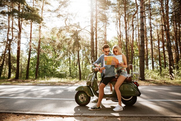 Heureux couple d'amoureux tenant la carte à l'extérieur près de scooter