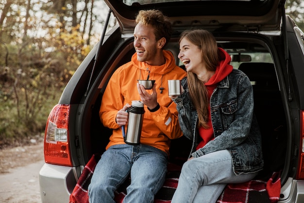 Heureux couple appréciant une boisson chaude dans le coffre de la voiture