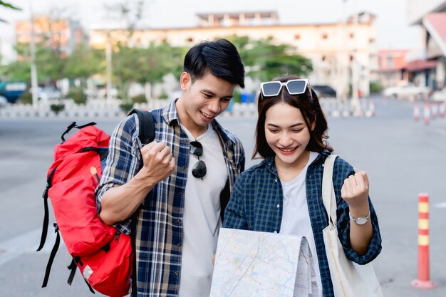 Heureux couple asiatique routards touristiques tenant une carte en papier et cherchant la direction tout en voyageant, ils sourient avec plaisir lorsqu'ils sont arrivés à l'emplacement sur la destination de la carte papier.