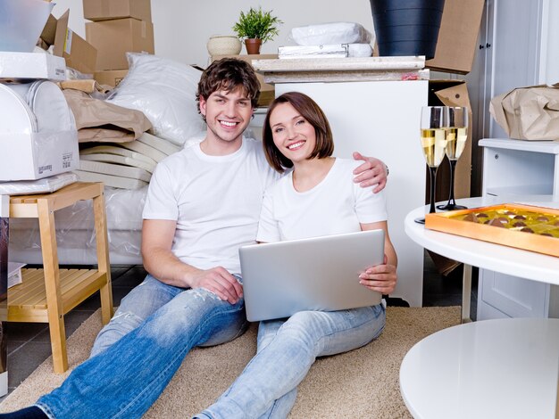 Heureux couple assis sur le sol avec un ordinateur portable après le déménagement
