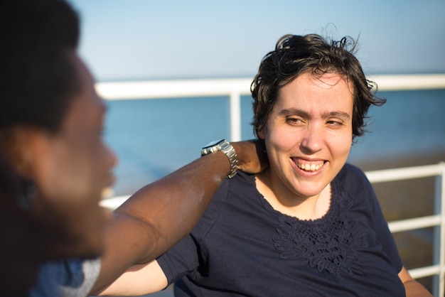 Photo gratuite heureux couple biracial marchant le jour de l'été. homme afro-américain et femme de race blanche en fauteuil roulant sur le remblai, se touchant les épaules. amour, relation, concept de bonheur