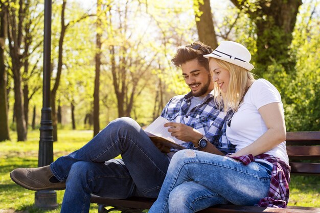 Heureux couple caucasien assis sur un banc de parc, lisant un livre ensemble