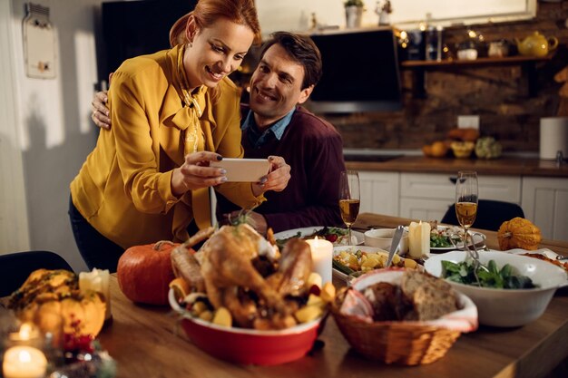 Heureux couple célébrant Thanksgiving et prenant une photo de la table à manger pour le dîner