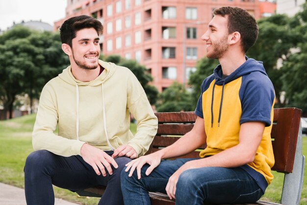 Heureux couple gay assis sur un banc en bois dans le parc