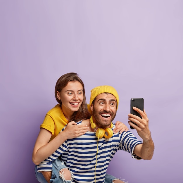 Heureux couple joyeux faire un portrait de selfie, un mec heureux donne ferroutage à sa petite amie, sourire largement