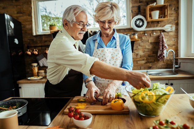 Heureux couple mature faisant de la salade tout en préparant la nourriture ensemble dans la cuisine.