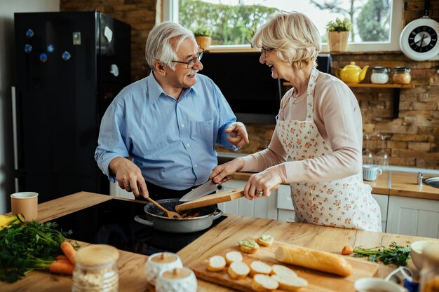 Heureux couple mature parler et s'amuser tout en cuisinant ensemble dans la cuisine