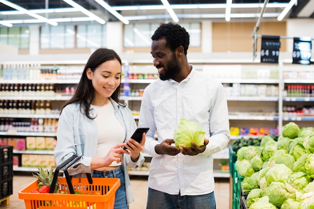 Heureux couple multiethnique choisissant des marchandises en supermarché