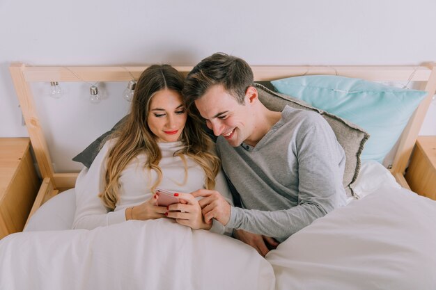 Heureux couple parcourant smarthone au lit