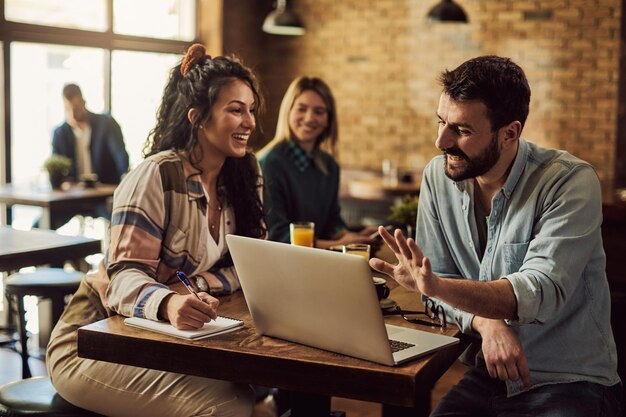 Heureux couple parlant tout en travaillant sur un ordinateur portable dans un café