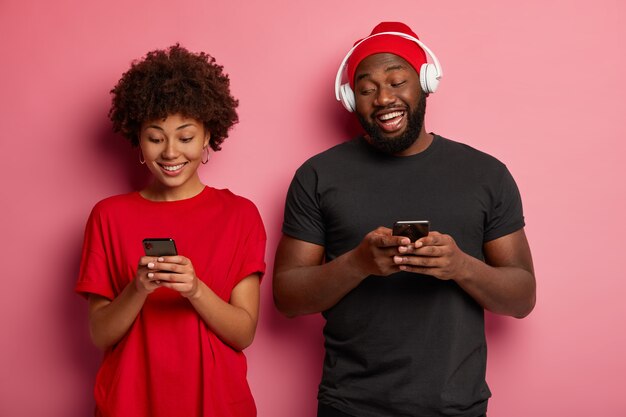 Heureux couple à la peau sombre se tient étroitement l'un à l'autre, accro aux technologies et gadgets modernes, joue à des jeux vidéo en ligne, a une bonne humeur