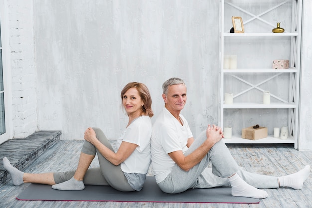 Heureux couple de personnes âgées assis dos à dos sur un tapis de yoga gris