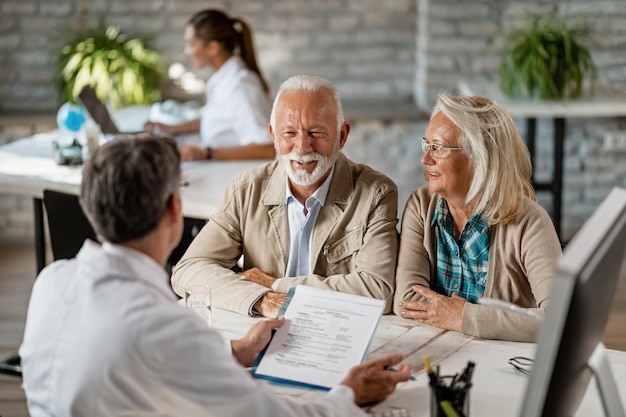 Heureux couple de personnes âgées communiquant avec un médecin au sujet de leur assurance maladie tout en passant par la paperasse