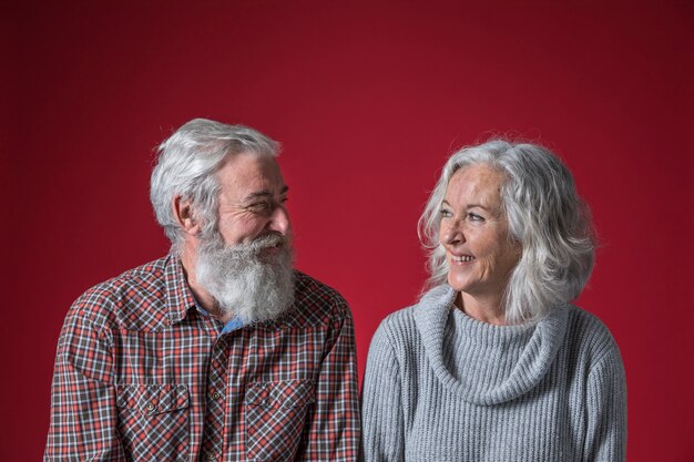 Heureux couple de personnes âgées à la recherche de l&#39;autre sur fond rouge