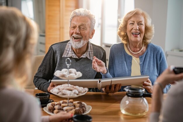 Heureux couple de personnes âgées s'amusant tout en communiquant avec leurs amis et en regardant l'album photo à la maison
