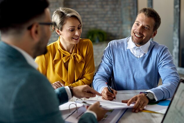 Heureux couple signant des documents lors d'une réunion avec un conseiller financier au bureau