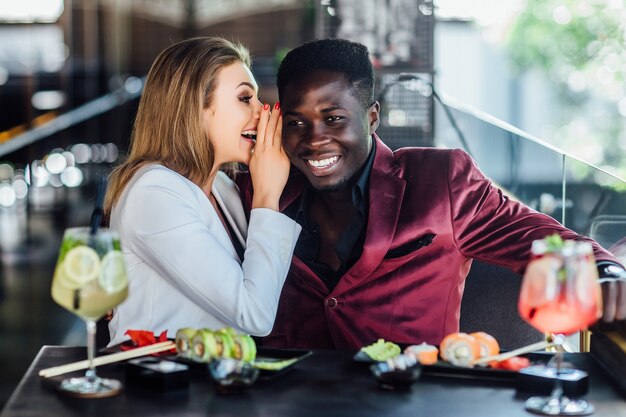 Heureux couple souriant de jeunes adultes se nourrissant de sushis au restaurant.