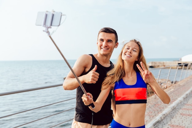 Heureux couple en sportswear montrant un pouce vers le haut et signe de paix tout en prenant un selfie