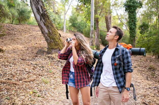 Heureux couple voyageant ensemble, prendre des photos et faire de la randonnée en forêt. Deux routards caucasiens marchant dans les bois. Femme tirant sur la nature à la caméra. Concept de tourisme, d'aventure et de vacances d'été