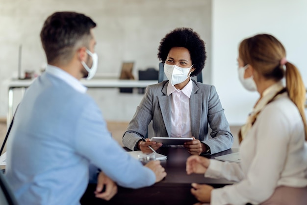 Heureux directeur de banque noir portant des masques faciaux tout en consultant un couple au bureau