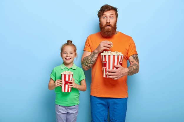 Heureux enfant aux cheveux roux et son papa tiennent des seaux de pop-corn savoureux