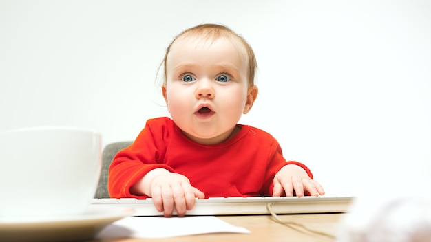 Heureux enfant bébé fille assise avec clavier d'ordinateur moderne ou ordinateur portable en blanc