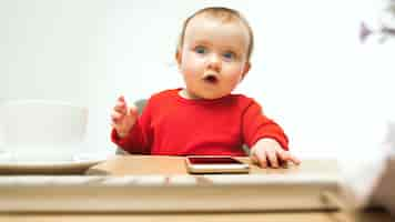 Photo gratuite heureux enfant bébé fille assise avec clavier d'ordinateur moderne ou ordinateur portable en studio blanc