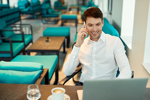 Heureux entrepreneur lisant et e-mail et parlant sur un téléphone portable assis dans un café