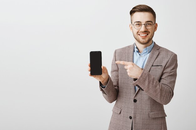 Heureux entrepreneur masculin en costume pointant le doigt sur les éboulis de smartphone, montrant l'application mobile