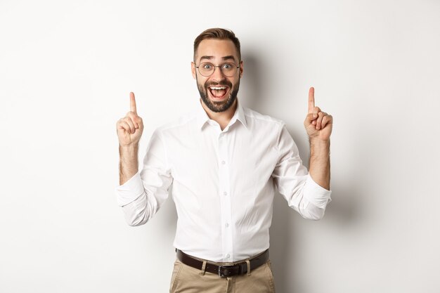 Heureux entrepreneur masculin en vêtements d'affaires, pointant du doigt vers le haut et montrant l'offre promotionnelle, debout