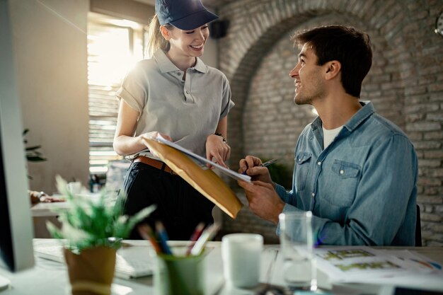 Heureux entrepreneur parlant avec une coursière lors de la signature d'une livraison au bureau